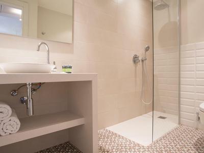 Moderne badkamer met glazen douche, wastafel, toilet en betegelde muren in neutrale kleuren.