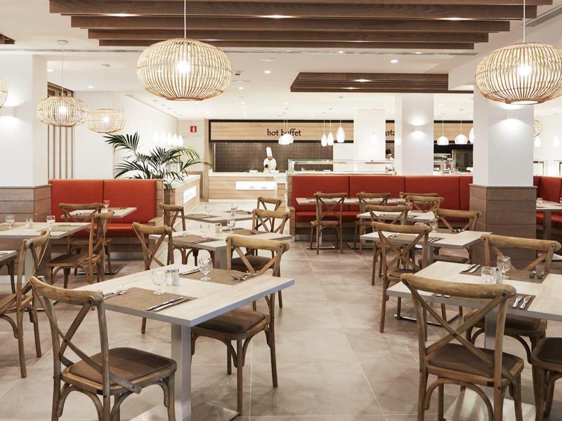 Elegant restaurant met houten tafels, stoelen en moderne verlichting in neutrale kleuren.