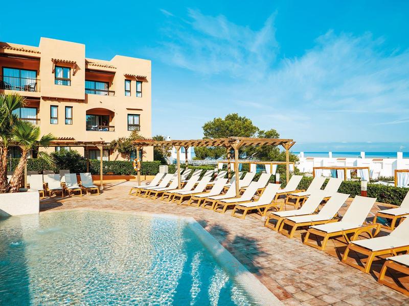 Hotelzwembad met ligstoelen en uitzicht op zee onder een blauwe lucht.