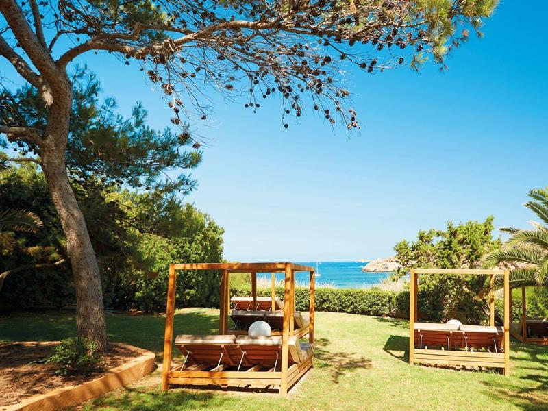 Twee overdekte ligbedden op gras met uitzicht op zee onder een heldere blauwe hemel.