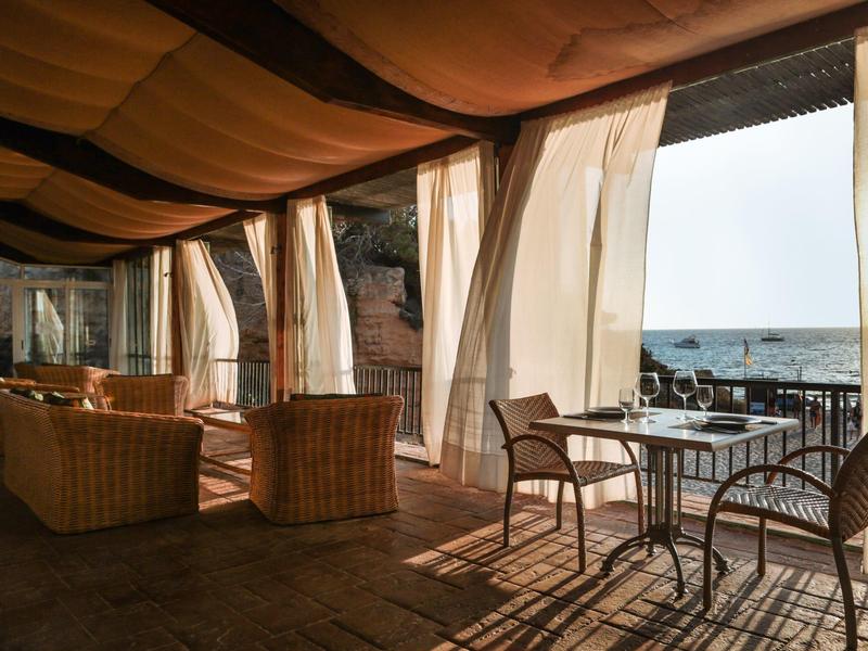 Terras met stoelen en tafels, zonnig uitzicht op de zee bij rustig weer.
