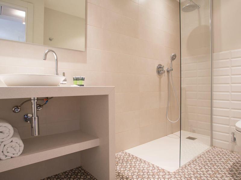 Moderne badkamer met glazen douche, wastafel, toilet en betegelde muren in neutrale kleuren.