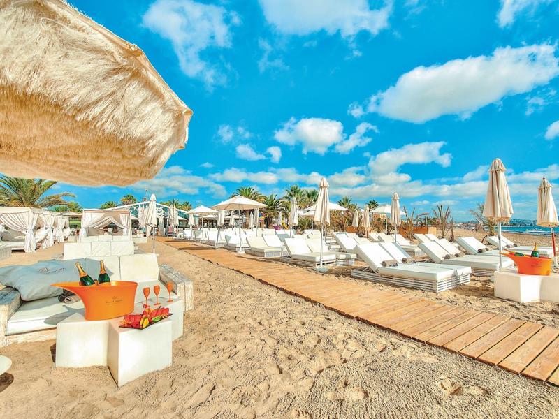 Piaszczysta plaża z leżakami i parasolami pod niebieskim niebem z chmurami.