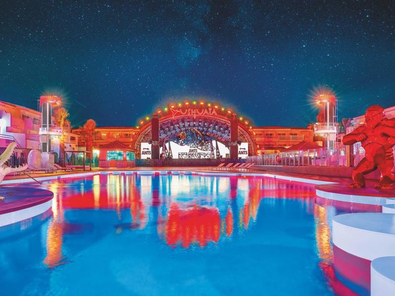 Oświetlony basen z rzeźbami i sceną w hotelu nocą.