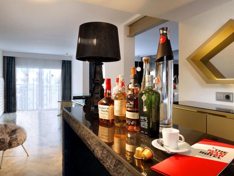 Elegancki bar hotelowy z butelkami, czarną lampą i miękkim fotelem przy oknie.