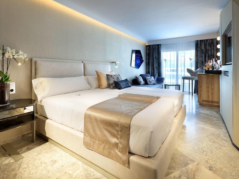 Nowoczesny pokój hotelowy z łóżkiem podwójnym, sofą i jasnym balkonem.