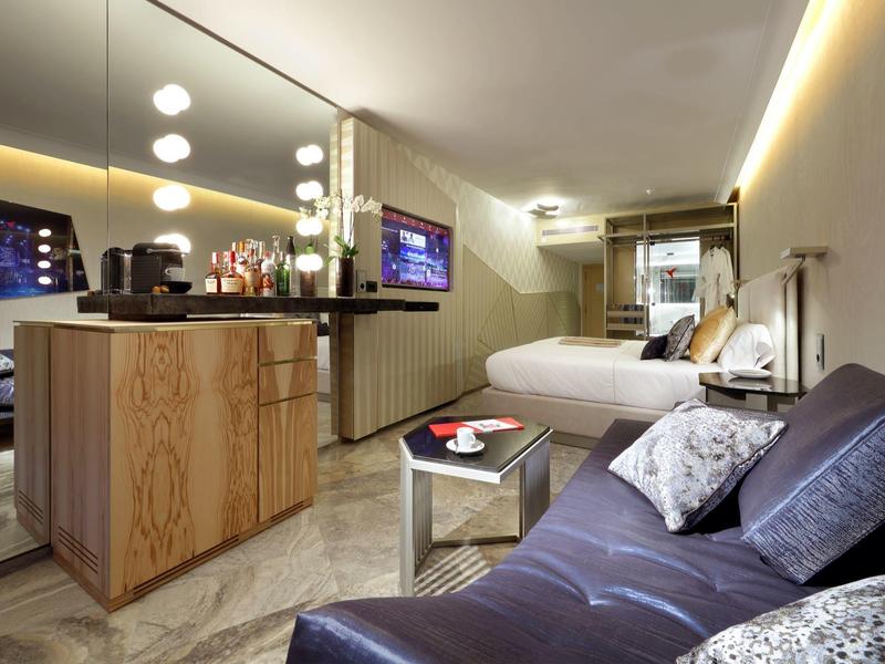 Nowoczesny pokój hotelowy z sofą, podwójnym łóżkiem i minibarem z jasnego drewna.