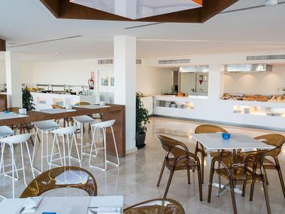 Restaurante moderno con paredes blancas, sillas de madera y metal, y pisos claros.