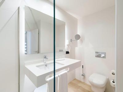 Jasna łazienka hotelowa z białą umywalką, toaletą i dużym lustrem.