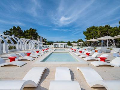 Nowoczesny basen z białymi leżakami i czerwonymi poduszkami pod niebieskim niebem.