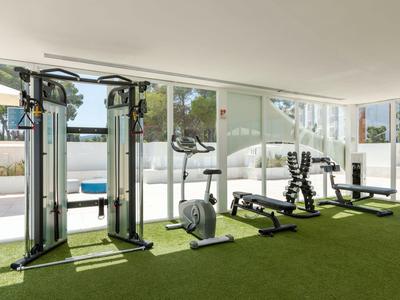 Gimnasio moderno con equipo de ejercicio, suelo de césped artificial verde y vista a la piscina.