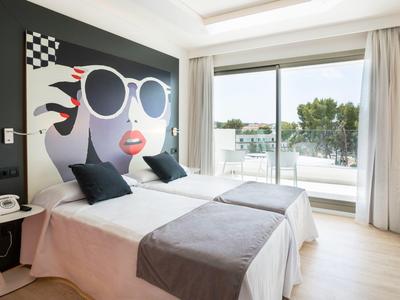 Modernes Hotelzimmer mit Doppelbett, großem Wandbild, Panoramafenster und Balkon mit Blick auf Bäume.