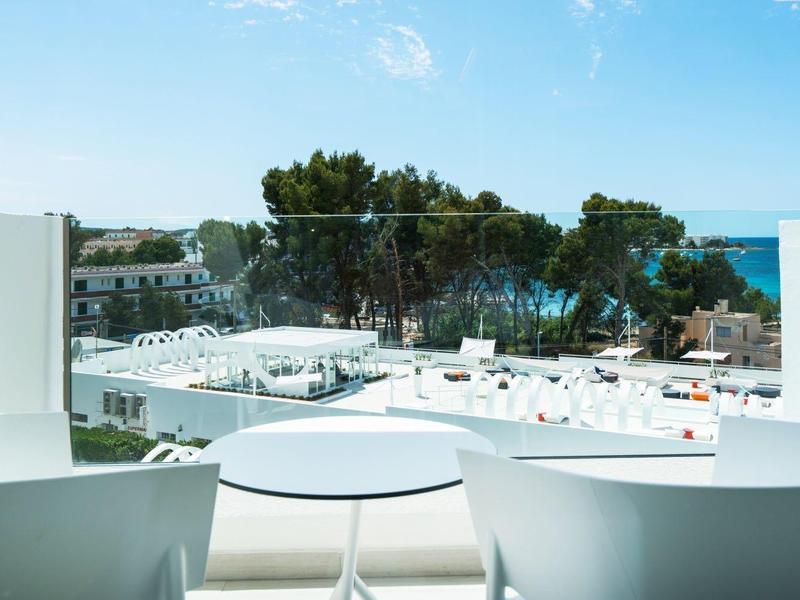 Taras z dwoma białymi krzesłami, widok na morze i białe dachy.