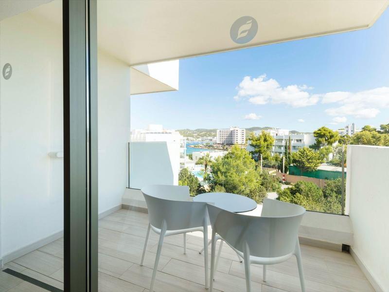 Balkon z małym stolikiem i dwoma krzesłami z widokiem na miasto i zieleń.