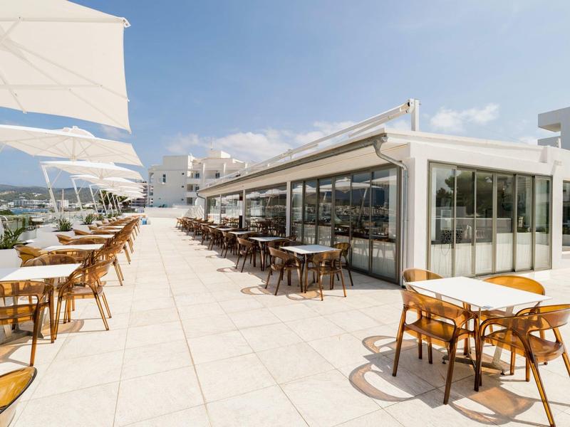 Taras hotelowy z stolikami i krzesłami w słoneczny dzień z widokiem na marinę.