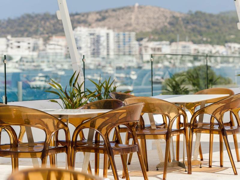 Puste drewniane stoły i krzesła na tarasie z widokiem na nadmorskie miasto.