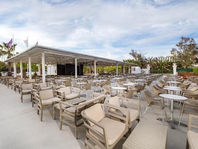 Große, offene Terrasse mit vielen beigen Sesseln und weißen Tischen unter einem Pavillon bei Tageslicht.