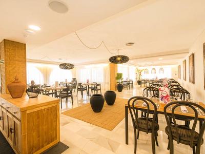 Helles Restaurant mit Holzstühlen, großen Fenstern und modernen Lampen an der Decke.