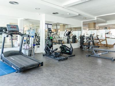 Moderner Fitnessraum mit Laufband, Fahrradergometer, Gewichten und großen Spiegeln.