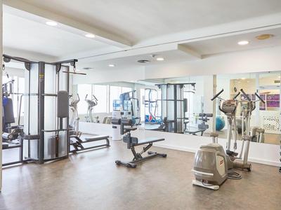 Heller Fitnessraum mit Geräten, Spiegelwand und Holzfußboden in modernem Design.
