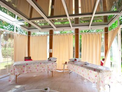 Helle Veranda mit Tischdecken bedeckten Tischen, beiger Gardinen und Holzbalkendach.