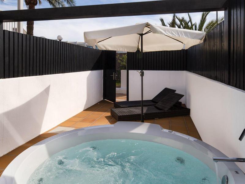 Ronde jacuzzi op een houten terras met ligstoelen en parasol in een moderne buitenruimte.