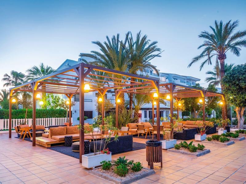 Verlichte terras met zitplaatsen en palmbomen bij een hotel tijdens schemering.