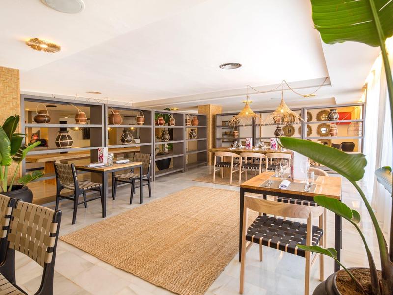 Licht, modern café met planten, rekken en houten stoelen in een ontspannen sfeer.