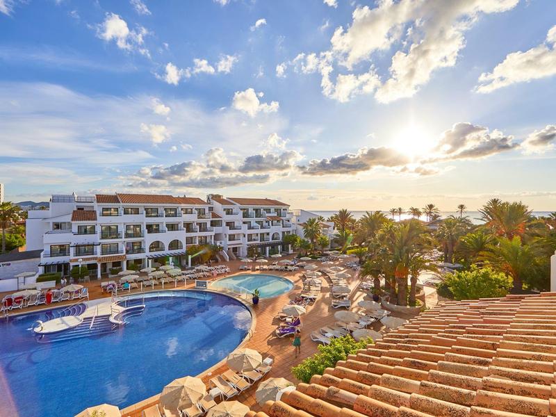 Hotel met grote zwembaden, zonnedekken en palmbomen bij zonsondergang.