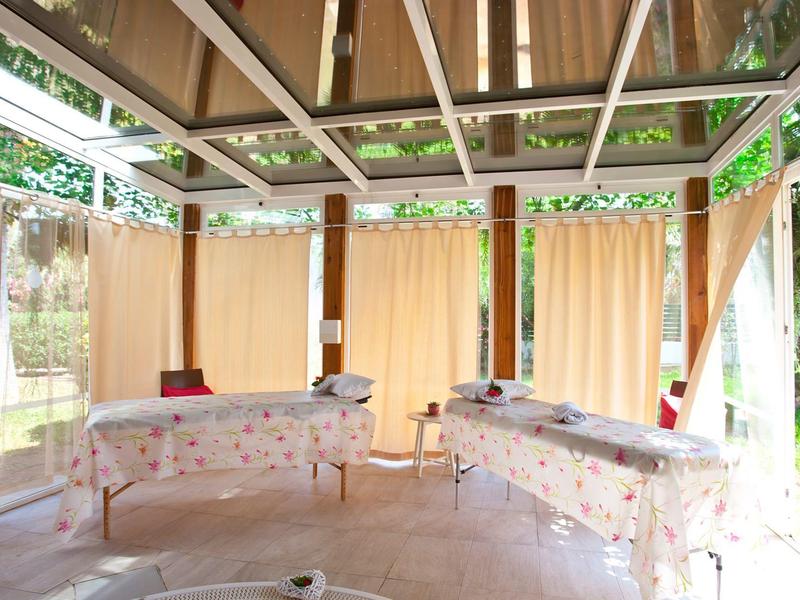 Licht wellnessruimte met twee massagetafels en grote ramen met gordijnen.