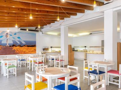 Lichte eetzaal met kleurrijke stoelen, houten balkenplafond en buffetgedeelte.