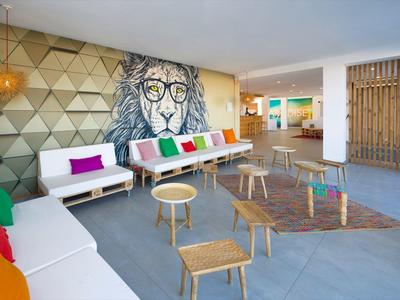 Moderner Aufenthaltsraum mit Löwenwandkunst, bunten Kissen und kleinen Holztischen.