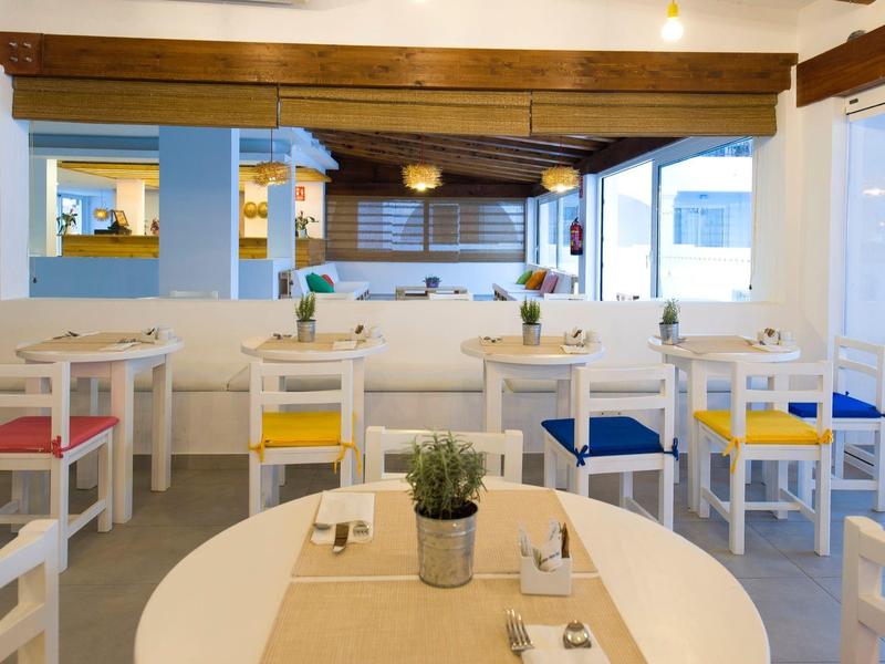 Lichte, moderne restaurantinterieur met witte tafels en kleurrijke kussens, planten op tafels.