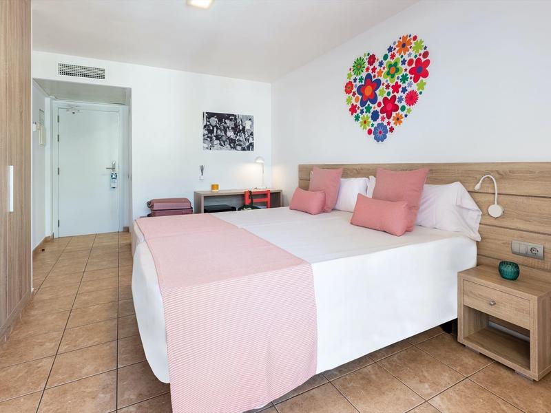 Moderne hotelkamer met tweepersoonsbed, kleurrijke hartdecoratie en houten meubels.