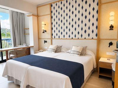 Lichte hotelkamer met tweepersoonsbed, patroonhoofdeinde en balkon toegang.