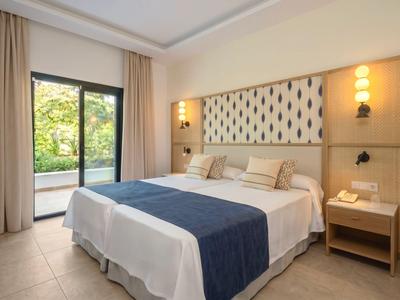Modern hotelkamer met tweepersoonsbed, nachtkastje, lichte gordijnen en uitzicht op groene natuur.