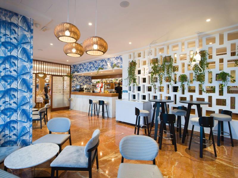 Modern hotel lounge area with seating groups, bar, and hanging plants on the wall.