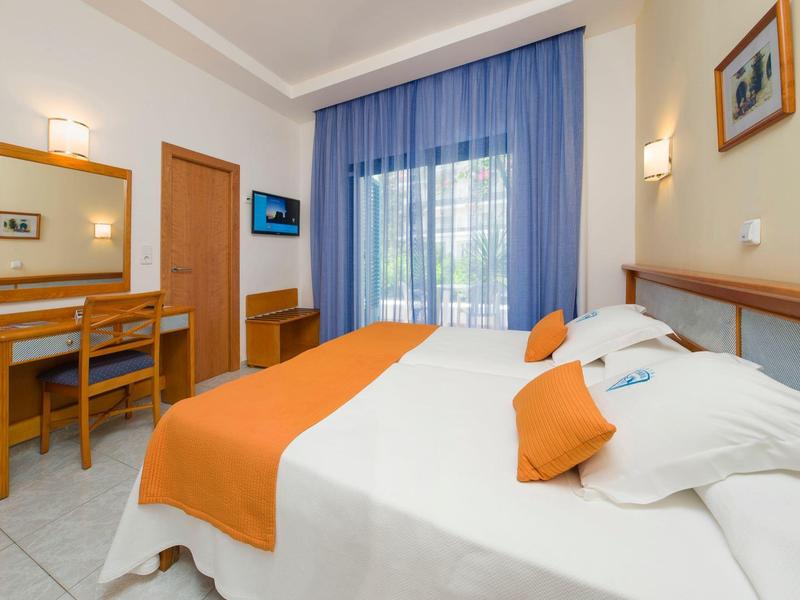 Cozy hotel room with double bed, orange bedding, and desk in front of blue curtains.