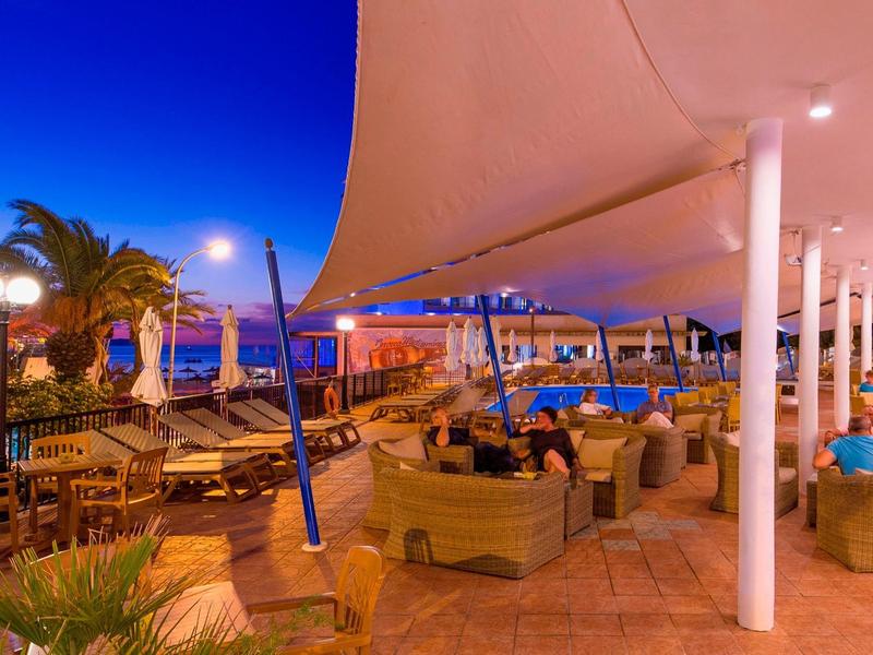 Illuminated hotel terrace with seating areas and pool at night.