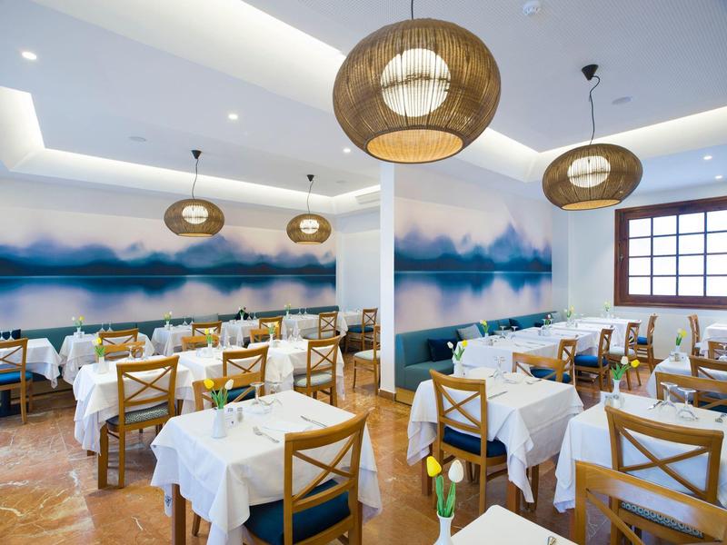 Bright restaurant with white tablecloths, wooden furniture, and modern round ceiling lights.