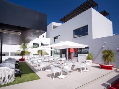 Modern hotel outdoor area with white furniture and umbrellas in bright sunlight.