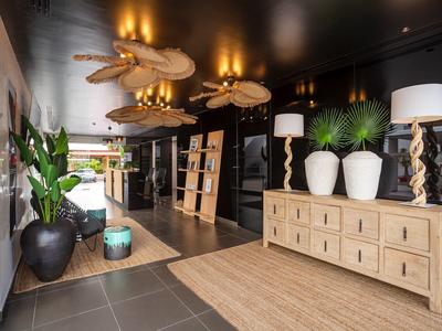 Modern hotel corridor with wooden cabinets, plants, and stylish lamps in warm lighting.