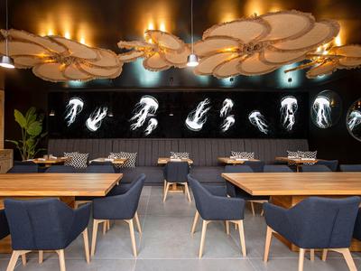 Modern restaurant with wooden tables, dark blue chairs, and striking ceiling lighting.
