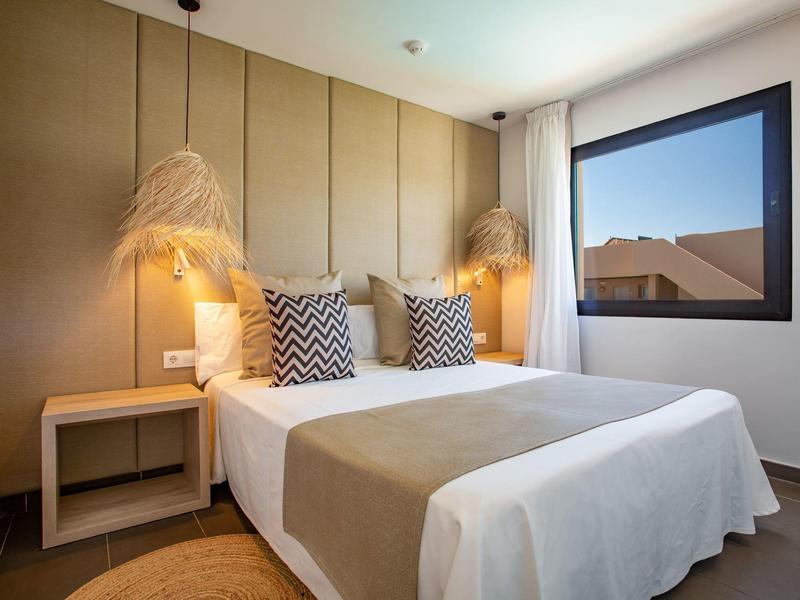 Modern hotel room with double bed, decorative pillows, and window overlooking rooftops.