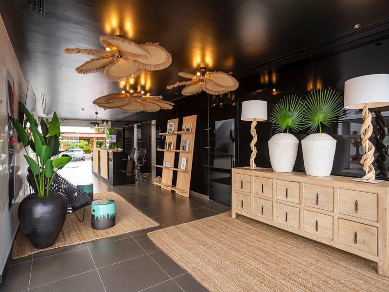 Modern hotel corridor with wooden cabinets, plants, and stylish lamps in warm lighting.
