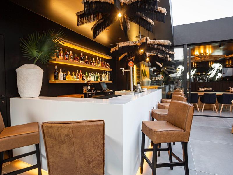 Modern hotel bar area with white counters, brown bar stools, and warm lighting ambiance.