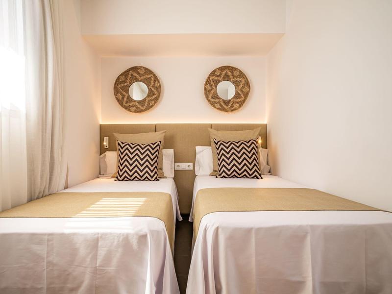 Two single beds with beige and white bedding and decorative pillows in a bright room.