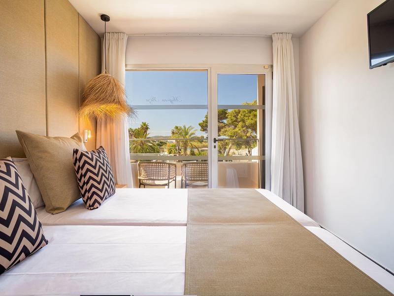 Modern hotel room with double bed, balcony, and sea view on a sunny day.