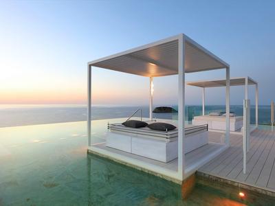 Twee witte tweepersoonsbedden met baldakijn bij een infinity pool met uitzicht op zee bij zonsondergang.