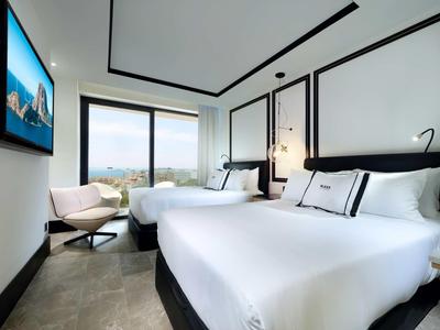 Modern hotel room with two beds, a large window, and a wall-mounted TV.